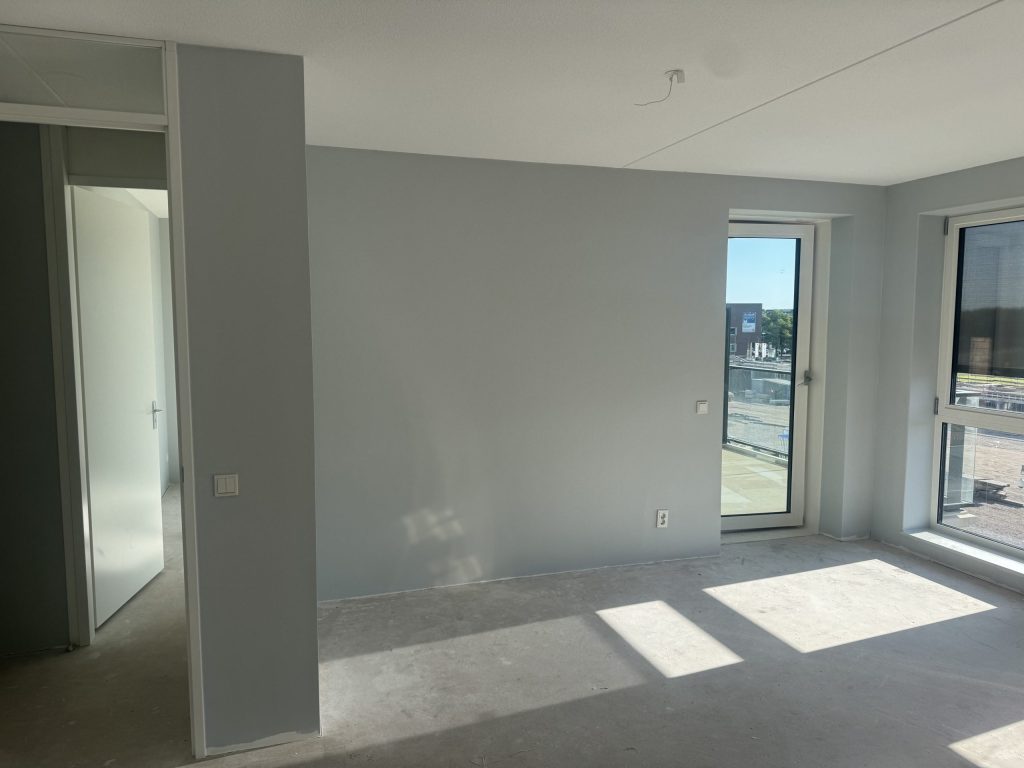 Pas opgeleverd appartement met lichtgrijze wanden, een balkondeur en een kale vloer
