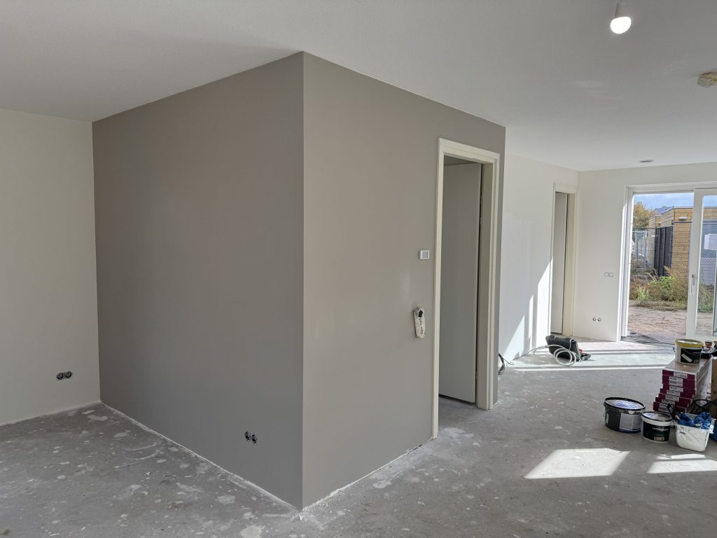 Open benedenverdieping met een taupe gesausde wand rond de trapkast en verfemmers bij de tuindeur